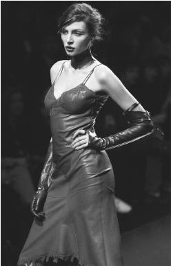 Model on catwalk posing in elbow lenght leather gloves and a fitted leather slip with lace trim by Lolita Lempicka