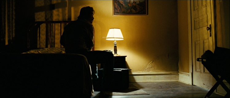 Still from the movie No Country for Old Men. A man sits on a hotel bed in darkness.